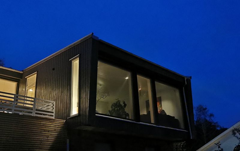 Hus fotografert i skumring med lys på inne, der man ser inn gjennom screenduken