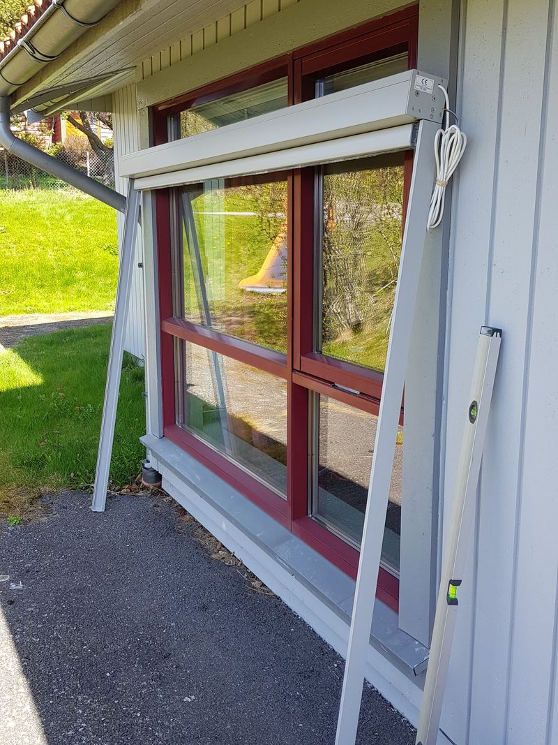 Kassett og sideskinner satt sammen og lent mot veggen under et vindu, klar til å løftes på plass